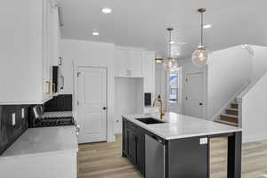 Kitchen featuring sink, white cabinetry, hanging light fixtures, appliances with stainless steel finishes, and an island with sink