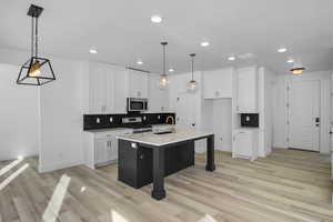 Kitchen featuring white cabinetry, appliances with stainless steel finishes, a center island with sink, and pendant lighting