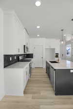 Kitchen with sink, light hardwood / wood-style flooring, appliances with stainless steel finishes, white cabinetry, and hanging light fixtures