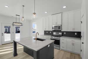 Kitchen with stainless steel appliances, white cabinetry, sink, and a kitchen island with sink