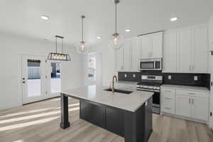 Kitchen featuring pendant lighting, sink, stainless steel appliances, white cabinets, and a center island with sink