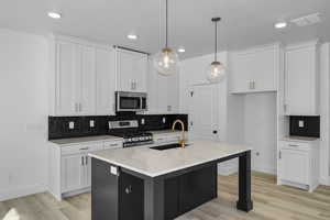 Kitchen featuring appliances with stainless steel finishes, sink, white cabinets, hanging light fixtures, and a kitchen island with sink