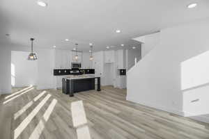 Kitchen with pendant lighting, a breakfast bar, white cabinetry, light hardwood / wood-style floors, and an island with sink