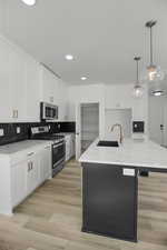 Kitchen with sink, appliances with stainless steel finishes, hanging light fixtures, white cabinets, and a center island with sink