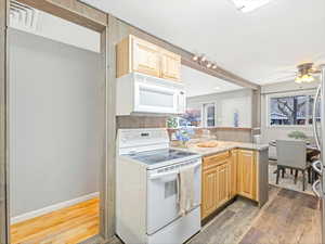 Kitchen with white appliances, wood-type flooring, light brown cabinetry, and plenty of natural light