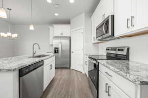 Kitchen with sink, an island with sink, pendant lighting, stainless steel appliances, and white cabinets