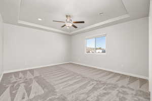 Carpeted spare room with a tray ceiling and ceiling fan