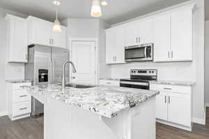 Kitchen with sink, appliances with stainless steel finishes, pendant lighting, a kitchen island with sink, and white cabinets