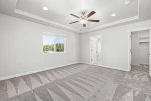 Unfurnished bedroom featuring a spacious closet, light colored carpet, ceiling fan, and a tray ceiling