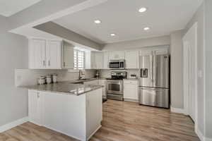 Kitchen with white cabinets, light stone counters, kitchen peninsula, stainless steel appliances, and light wood-type flooring