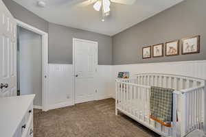 Bedroom with a nursery area, ceiling fan, and dark colored carpet