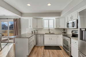 Kitchen featuring appliances with stainless steel finishes, white cabinetry, sink, light hardwood / wood-style floors, and kitchen peninsula