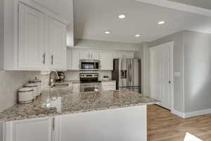 Kitchen featuring sink, light stone counters, appliances with stainless steel finishes, white cabinets, and backsplash