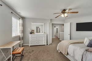 Carpeted bedroom featuring ensuite bath and ceiling fan