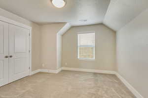 Bonus room with vaulted ceiling, light carpet, and a textured ceiling