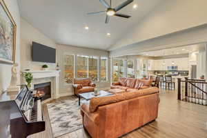 Living room with ceiling fan, a tiled fireplace, high vaulted ceiling, and light wood-type flooring