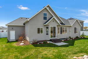 Rear view of property with fence, a shingled roof, a lawn, and stucco siding