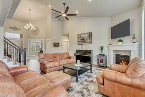 Living room featuring high vaulted ceiling, ceiling fan with notable chandelier, and a fireplace