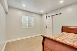 Unfurnished bedroom with a barn door and light carpet