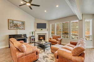 Living room with lofted ceiling with beams, a tiled fireplace, and ceiling fan