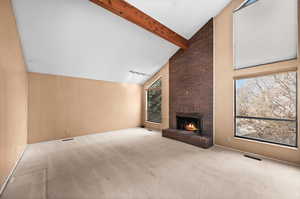 Living room with beamed ceiling, light colored carpet, a fireplace, and high vaulted ceiling