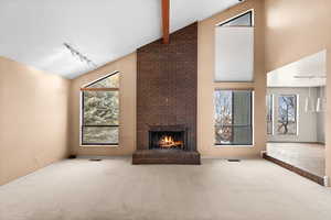 Living room featuring beamed ceiling, rail lighting, carpet floors, and a brick fireplace