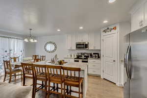 Kitchen featuring sink, appliances with stainless steel finishes, light stone counters, white cabinets, and decorative light fixtures