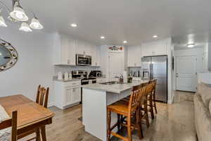 Kitchen with decorative light fixtures, white cabinetry, sink, stainless steel appliances, and light stone countertops