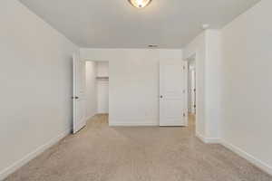 Unfurnished bedroom with a walk in closet and light carpet