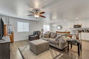 Living room with ceiling fan with notable chandelier and light wood-type flooring