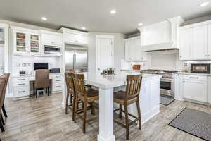 Kitchen featuring white cabinetry, premium range hood, built in appliances, and light hardwood / wood-style flooring