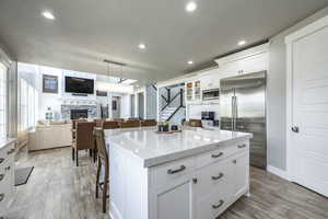 Kitchen with white cabinetry, a kitchen island, built in appliances, and a stone fireplace