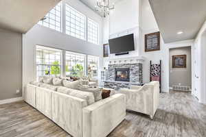 Living room with wood-type flooring, a stone fireplace, a chandelier, and a textured ceiling