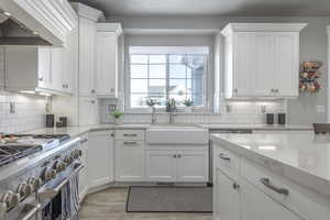 Kitchen featuring white cabinetry, light stone countertops, high end stove, and sink