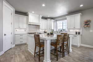 Kitchen featuring light hardwood / wood-style flooring, a center island, white cabinets, and a kitchen bar