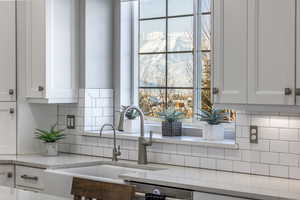 Kitchen with tasteful backsplash, white cabinetry, sink, and light stone counters