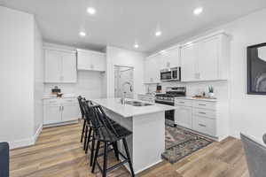 Kitchen with a breakfast bar, sink, white cabinets, a kitchen island with sink, and stainless steel appliances