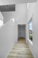 Hallway with light hardwood / wood-style flooring and a high ceiling