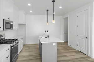 Kitchen with sink, decorative light fixtures, a center island with sink, stainless steel appliances, and white cabinets