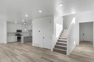 Kitchen with light hardwood / wood-style flooring, appliances with stainless steel finishes, white cabinetry, an island with sink, and decorative light fixtures