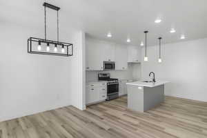 Kitchen with sink, stainless steel appliances, an island with sink, white cabinets, and decorative light fixtures