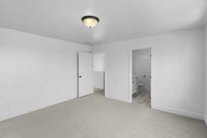 Unfurnished bedroom with ensuite bath and light colored carpet