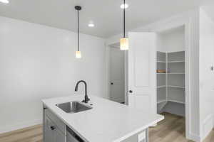 Kitchen featuring sink, decorative light fixtures, light wood-type flooring, and a center island with sink