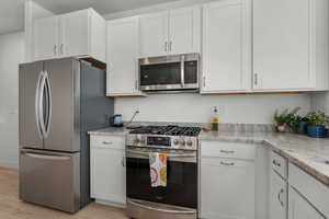 Kitchen featuring light stone counters, stainless steel appliances, light laminate flooring, and white cabinets