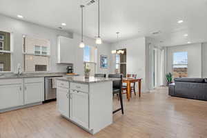 Kitchen featuring pendant lighting, dishwasher, sink, white cabinets, and a center island