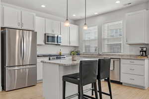 Kitchen featuring light stone counters, white cabinets, large island and appliances with stainless steel finishes