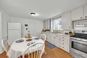 Kitchen featuring sink, white cabinetry, white refrigerator, light hardwood / wood-style floors, and gas range