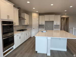 Kitchen with a kitchen island with sink, white cabinetry, and wall chimney exhaust hood