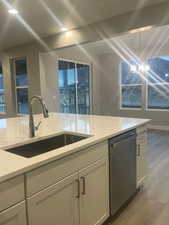 Kitchen with dishwasher, sink, hanging light fixtures, light stone countertops, and light wood-type flooring