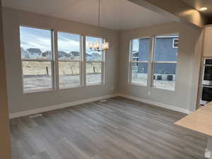 Unfurnished dining area with an inviting chandelier and light hardwood / wood-style floors